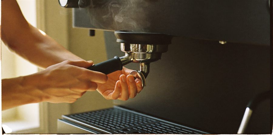 Hænder der låser en portafilter fast i espressomaskinen mens dampen stiger.