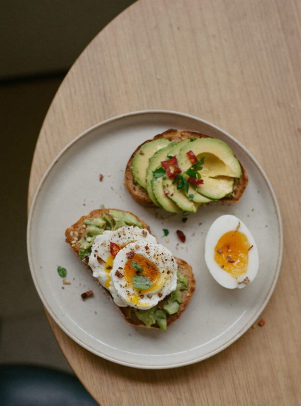 Surdejstoast med avocado, et blødt pocheret æg og chiliflager på en flødefarvet tallerken.