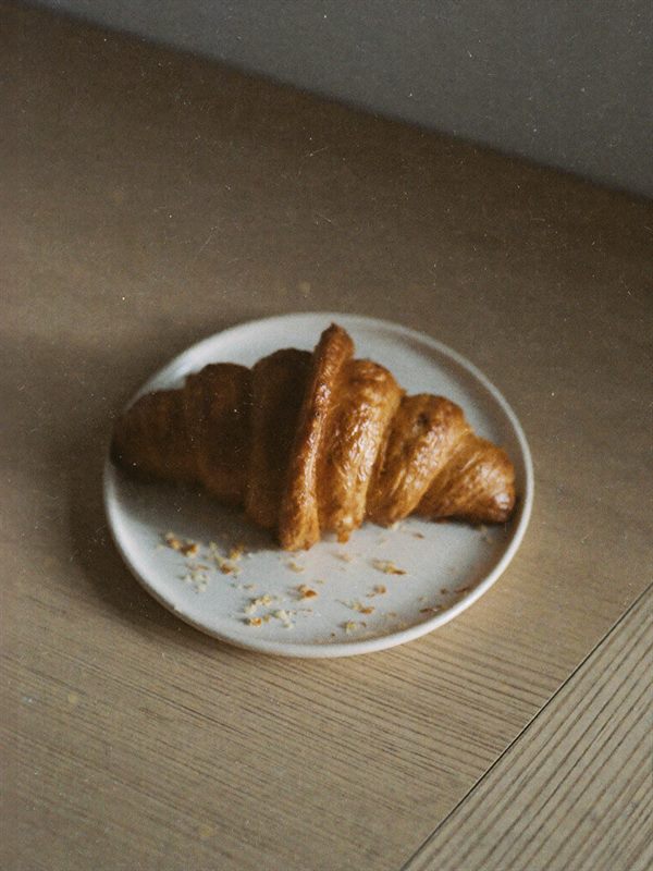 En gylden smørcroissant med tydelige lag på en lille flødefarvet tallerken.