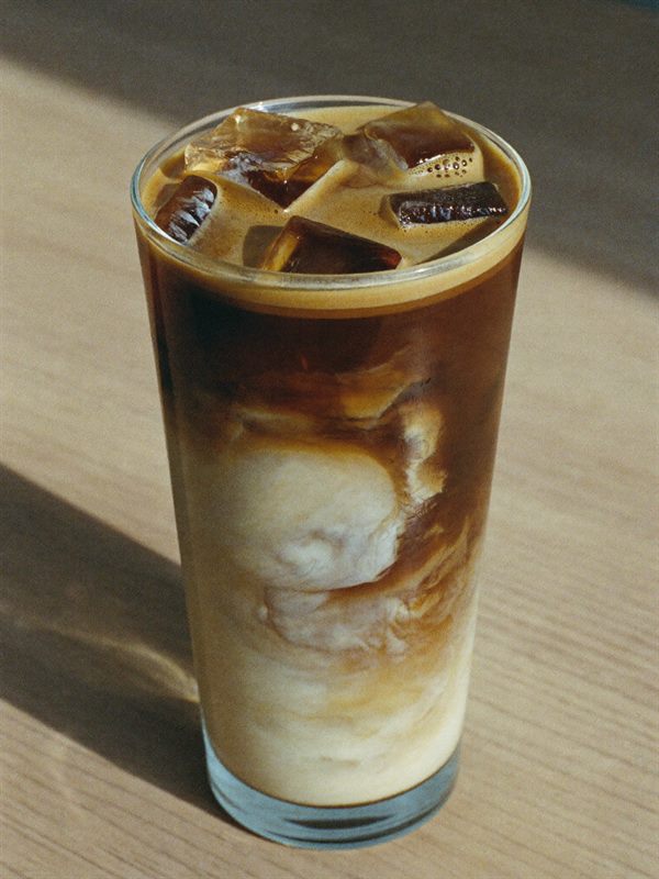 Iskaffe på filter i et højt glas med fløde der hvirvler igennem.