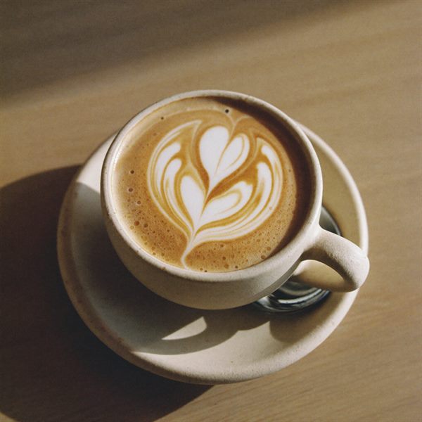 En flat white i en flødefarvet stentøjskop med en rosetta hældt i overfladen.